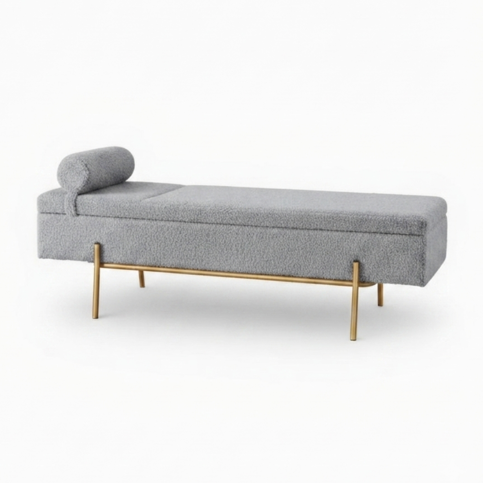 A modern chaise lounge bench upholstered in textured light gray fabric, featuring a cylindrical matching headrest and slim gold metal legs, shown against a plain white background.