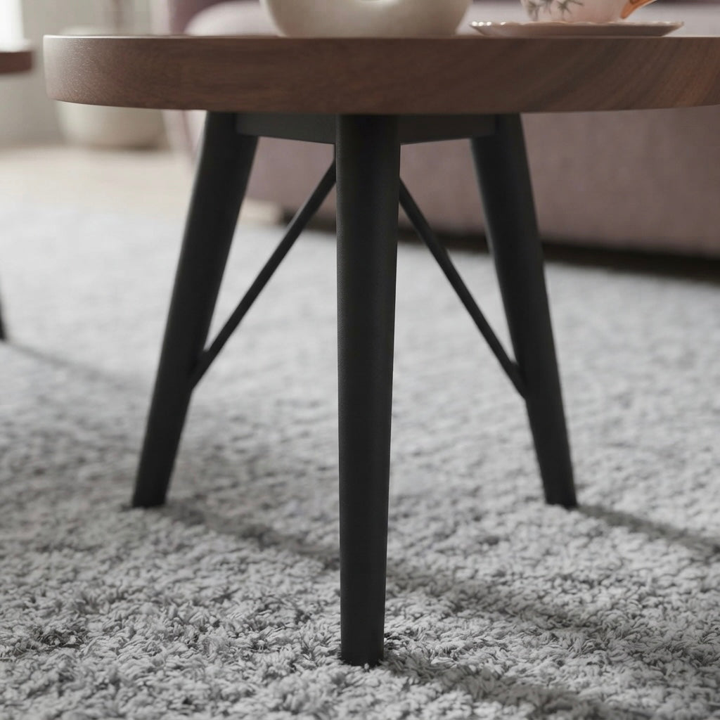 A close-up of a round wooden coffee table with black metal legs, set on a light gray shag rug in a living room setting.